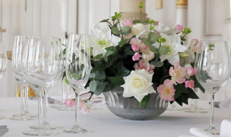Low arrangement of white roses and pink flowers in a zinc bowl, among glasses