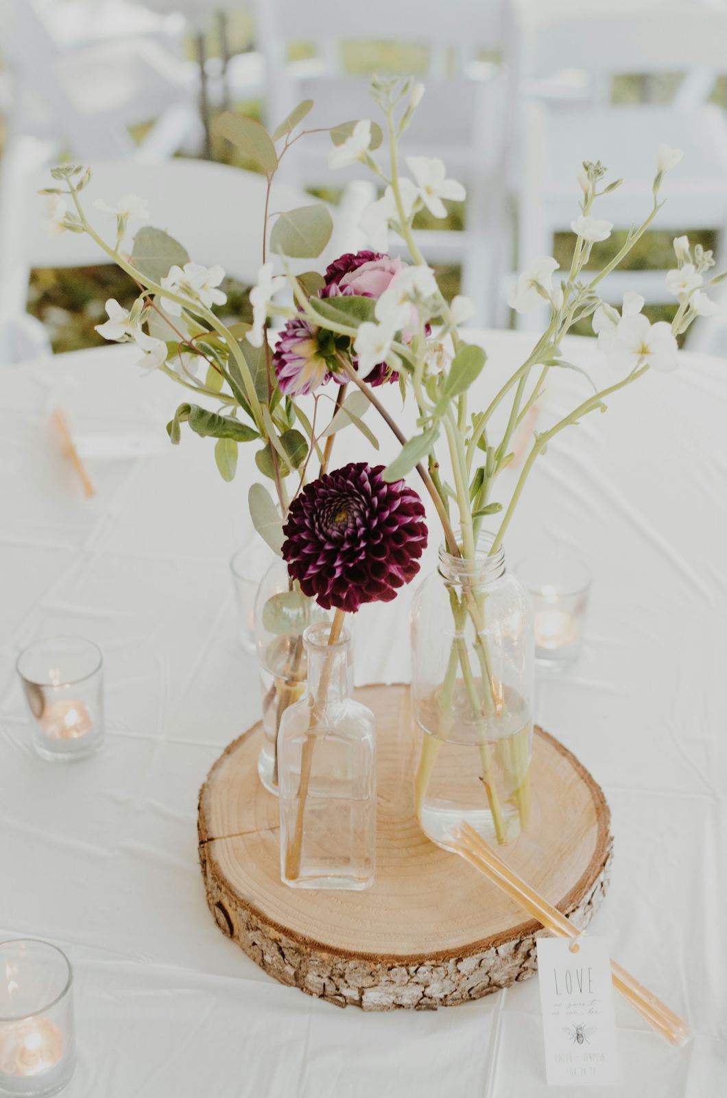 A deep red dahlia and wildflowers in glass bottles on a log slice