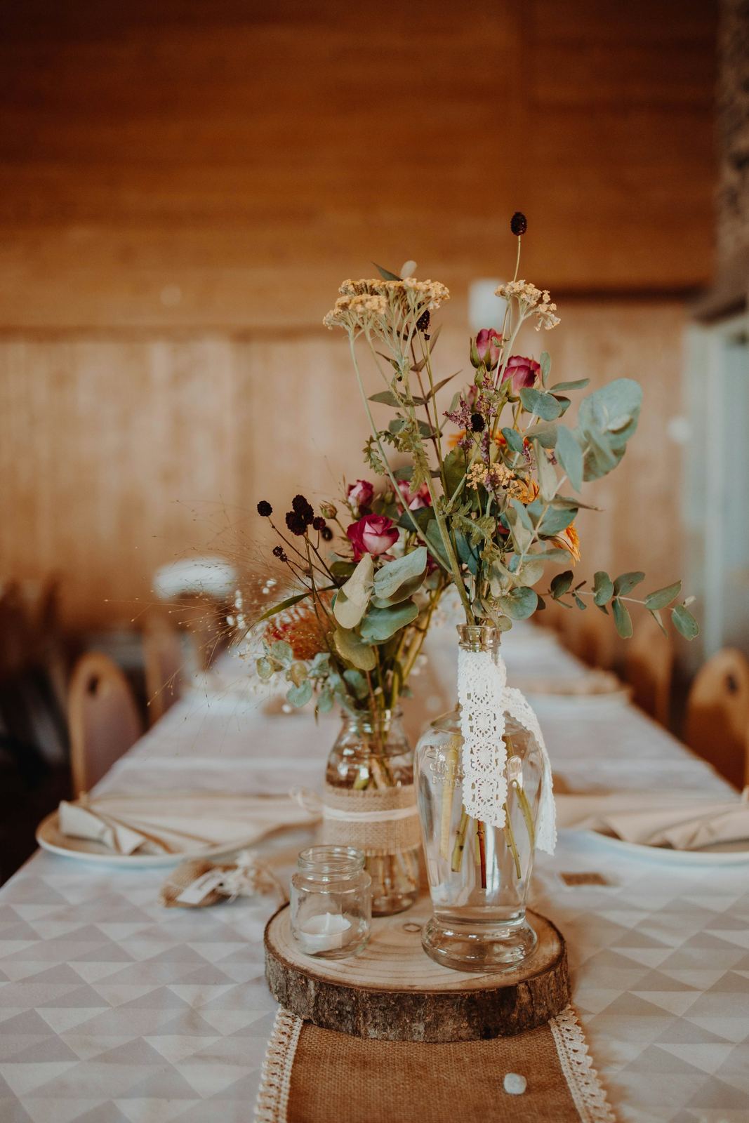 Glass bottles with wildflowers and lace on a log slice, on a long banquet table