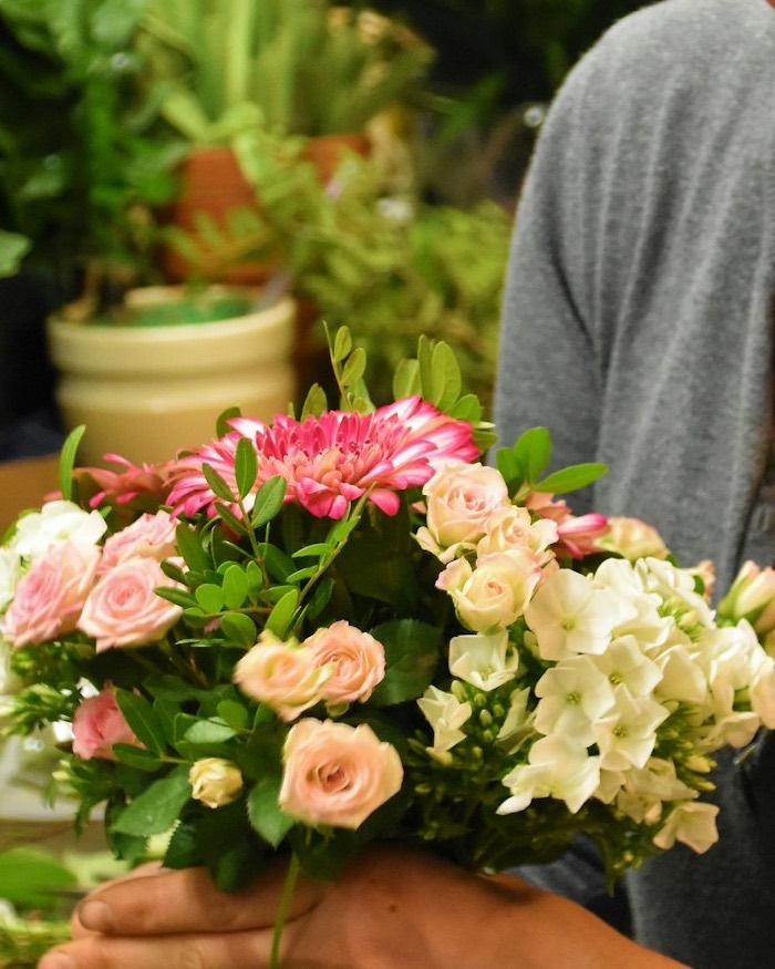 Hands holding a round bouquet of pink roses, gerbera and white flowers