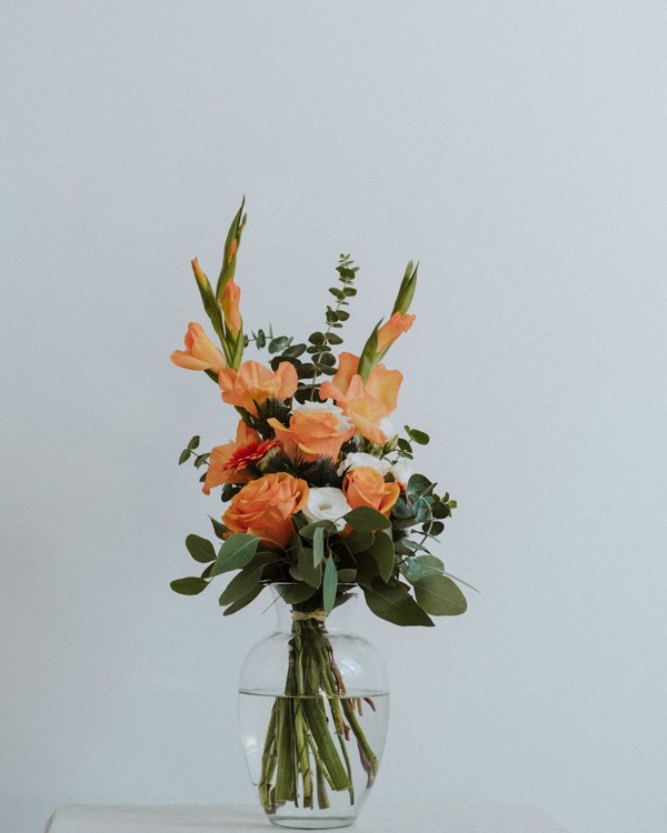 Orange and pink gladioli with eucalyptus in a glass vase