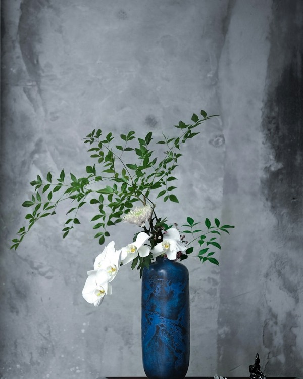 White orchid with green branches in a blue vase