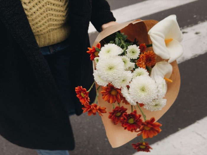 Bouquet of white and orange chrysanthemums with calla lilies in kraft paper, being carried across the street