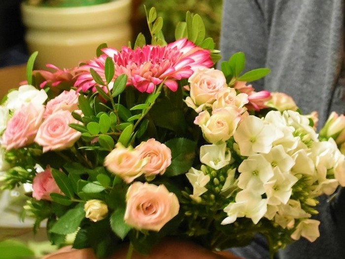 Ramo redondo de rosas, gerbera y flor blanca en las manos